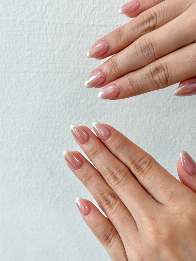Soft pink nude almond nails against a white wall